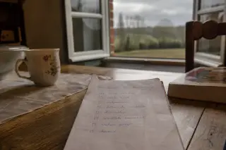 Checklist on rustic wooden table near window with soft Normandy light and countryside outside, evoking calm preparation before radiotherapy.