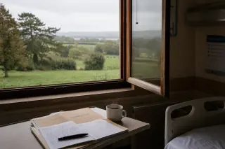 Open hospital window in Normandy overlooking misty bocage, with a medical file and coffee cup on the ledge, in soft natural light.